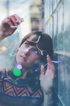 A young lady holding a string of colored mini lights standing next to a wall