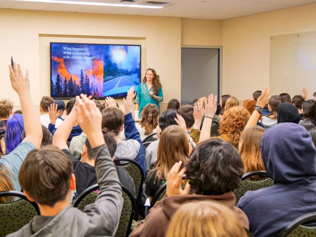 A group of youth sitting and raising their hands during a presentation on climate change.