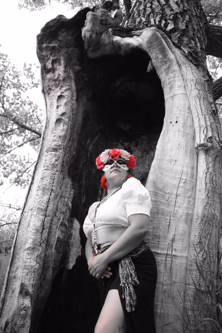 Singer LatinSoul with a mask on her face standing in front of a large tree trunk